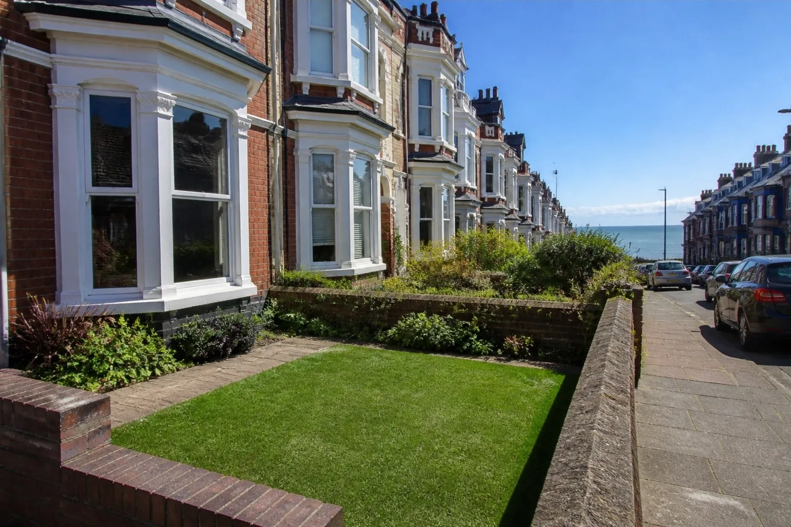 Bay-windowed seaside terraces with small front lawns behind low walls and the sea at the end of the street