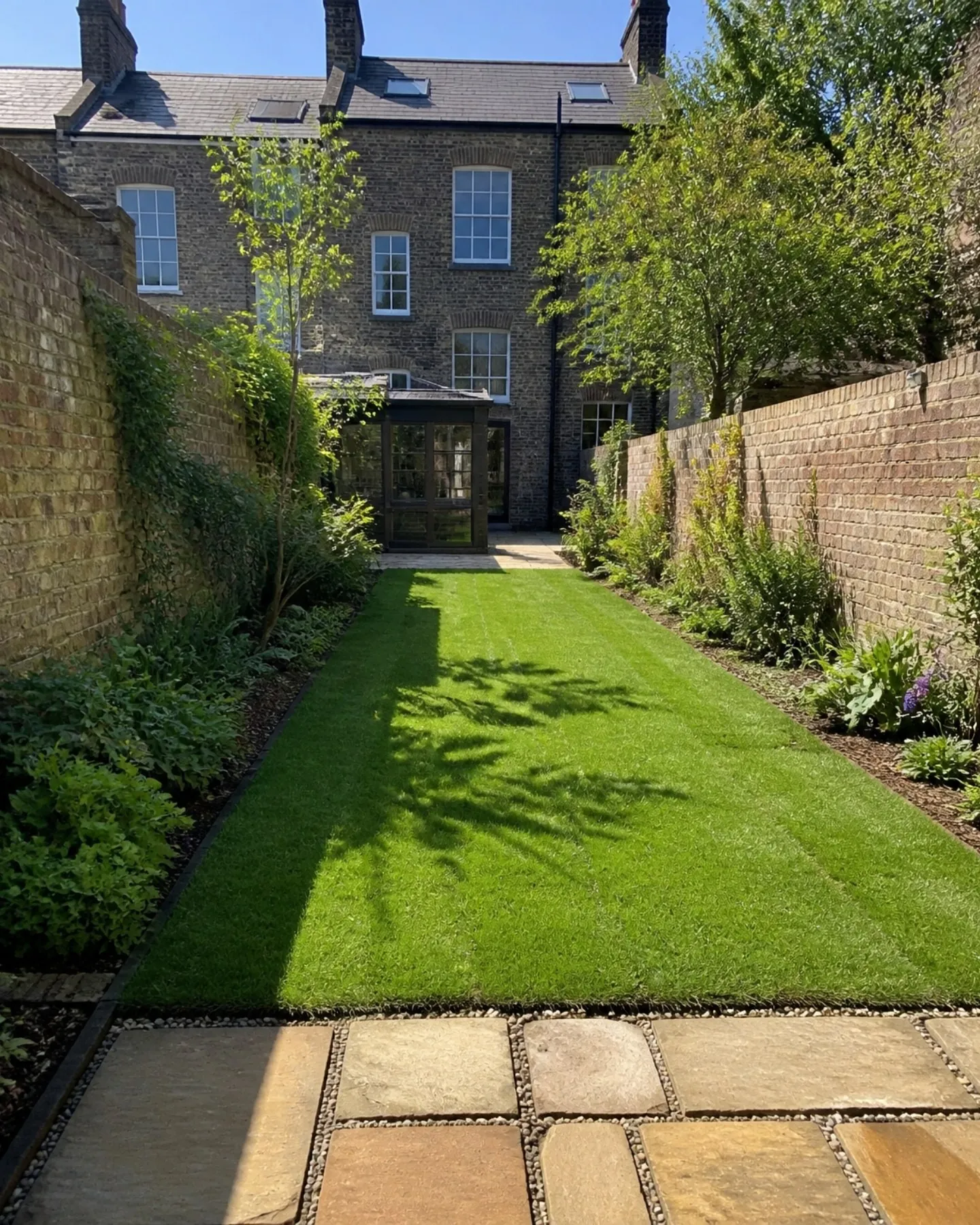 Long walled back garden of a tall Victorian terrace with a new lawn and a stone-flag path