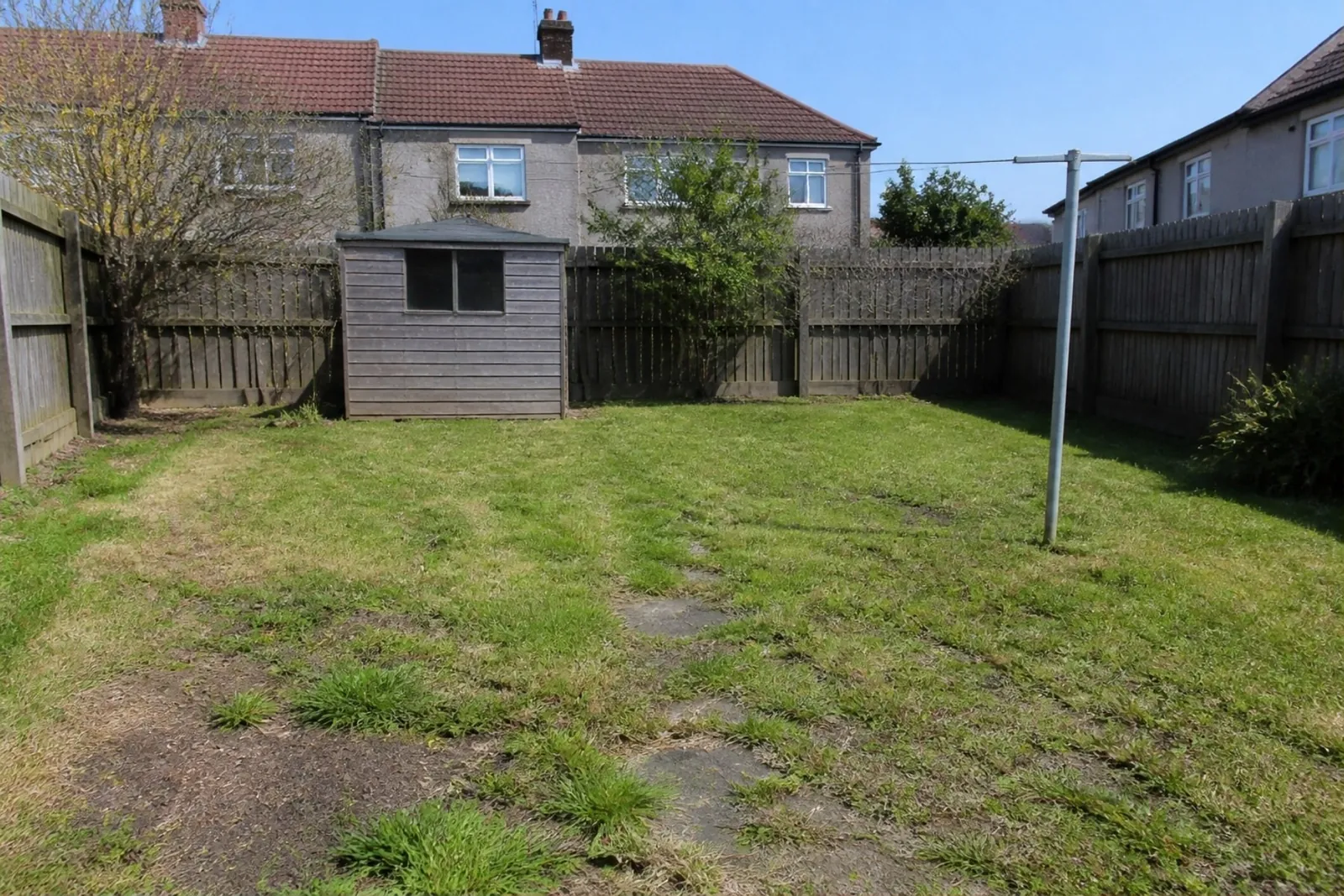Worn, patchy lawn with moss and bare soil behind a 1960s semi, with a shed and washing line